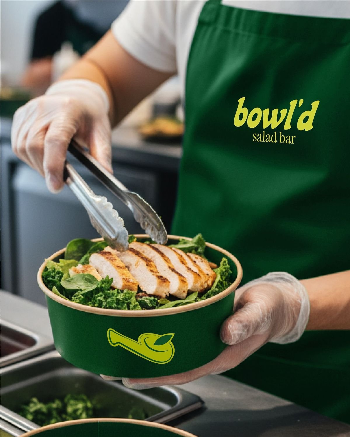 Identité Bowl'd Salad Bar appliquée au tablier et au packaging d’un bowl