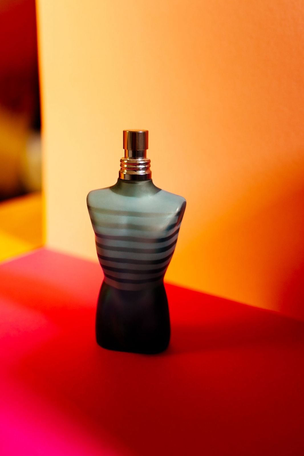 Flacon de parfum photographié dans une composition orange et rouge